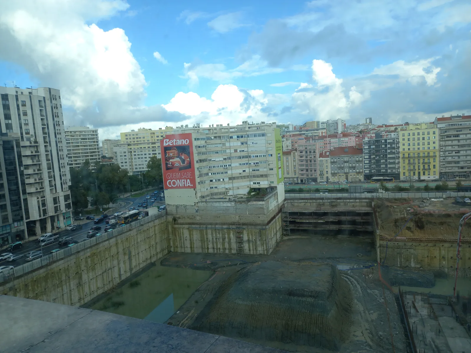 Escavação e estruturas de contenção num estaleiro em Entrecampos, rodeado por edifícios de Lisboa.