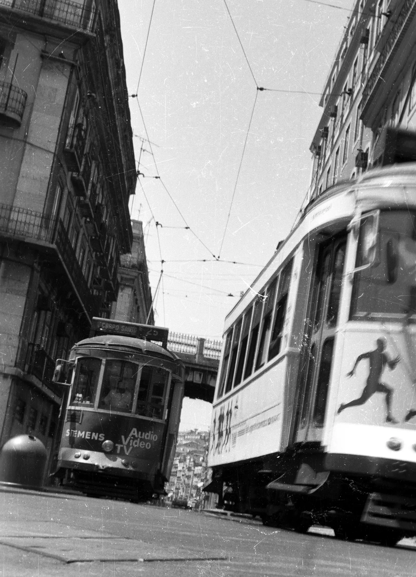 Dois elétricos entre fachadas de edifícios da Rua de São Paulo, numa fotografia a preto e branco de Lisboa em 1990.