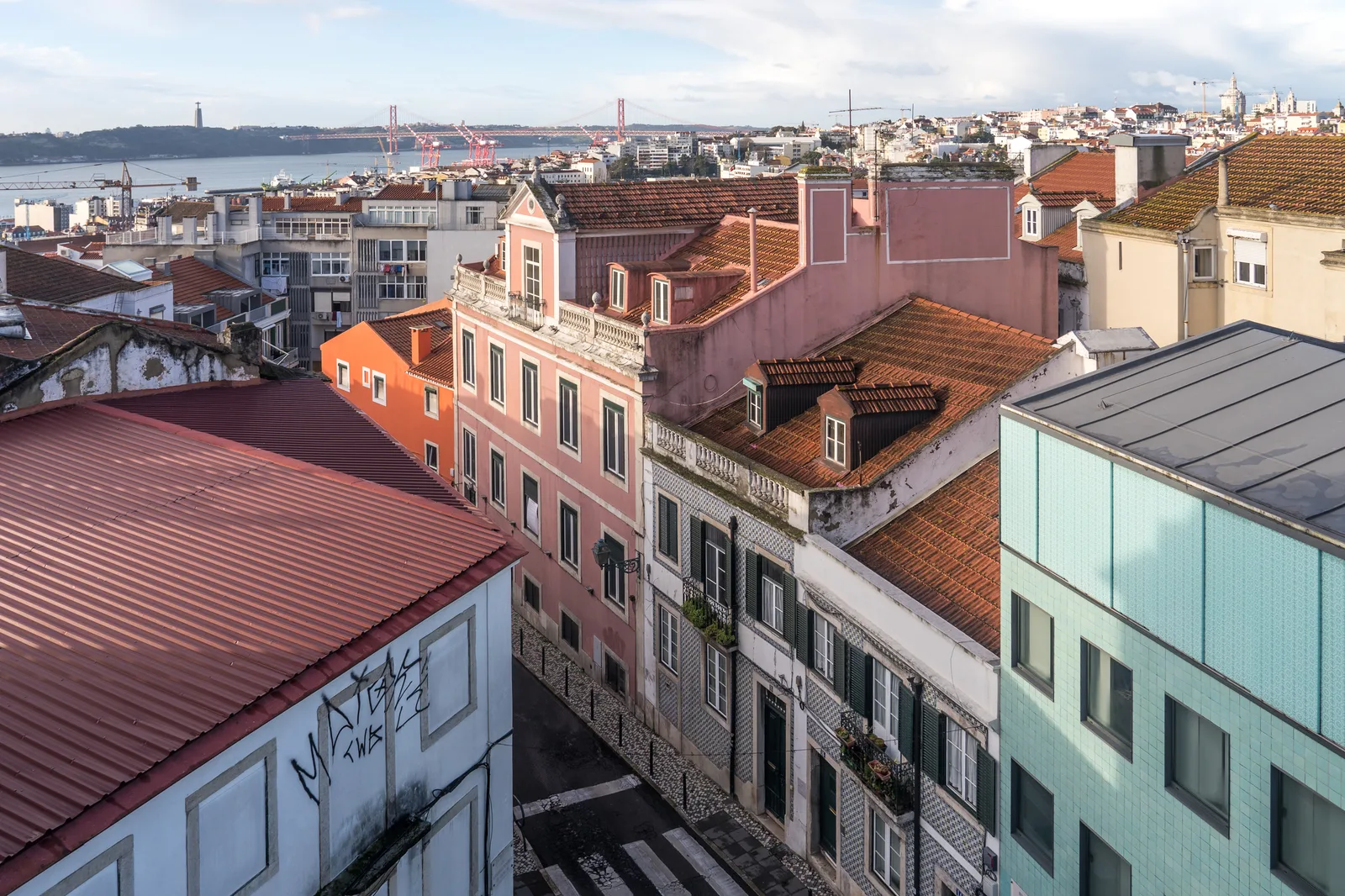 Vista de telhados e fachadas de Lisboa a partir da Rua da Palmeira, com o Tejo ao fundo.